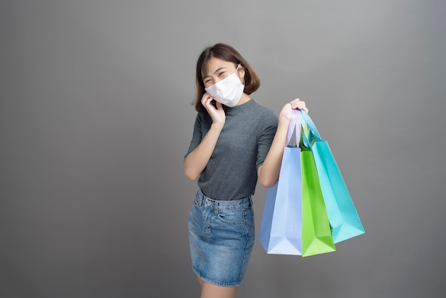 A portrait of young beautiful asian woman wearing a surgical mak is holding credit card and colorful shopping bag isolated