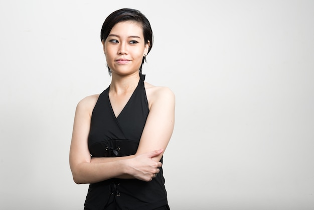 Portrait of young beautiful Asian woman with short hair against white wall