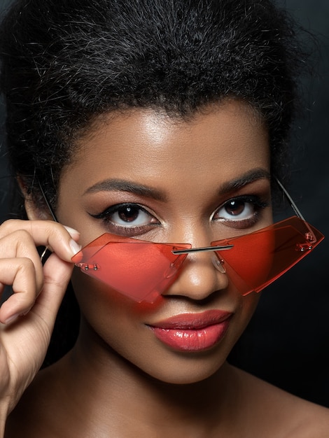 Portrait of young beautiful black woman looking over modern fashion red sunglasses