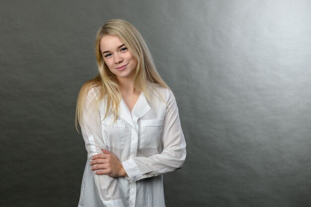 Portrait of young beautiful blonde businesswoman smiling on grey background. Copy space.