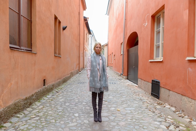 Портрет молодой красивой блондинки скандинавской женщины вдоль аллеи с оранжевым зданием в городе