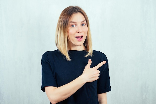 若くて美しいブロンドの女性の肖像画は、黒いTシャツで指を指しています