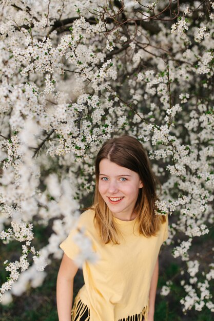 Portrait of young beautiful blonde woman near blooming tree with white flowers on a sunny day