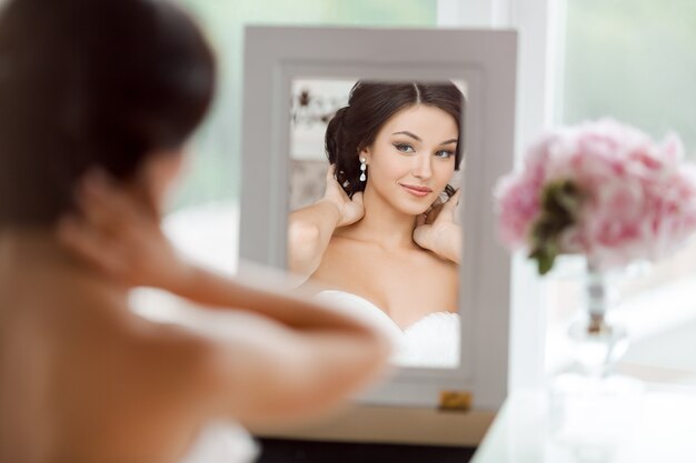 Portrait of the young beautiful bride looks at herself in the mirror