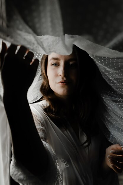 Portrait of a young and beautiful bride during the morning preparations on the wedding day. beautiful girl holds a veil on her head. wedding morning of the bride.