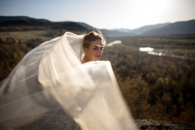 ベールが付いている山の若い美しい花嫁の肖像画。風がベールを作ります。山での結婚式の写真。