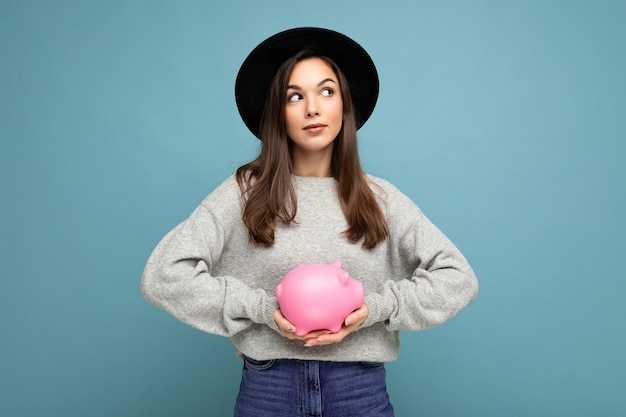 Portrait of young beautiful brunette woman wearing stylish gray sweater and black hat isolated over