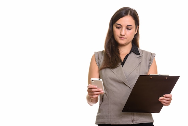 Portrait of young beautiful businesswoman using phone while holding clipboard