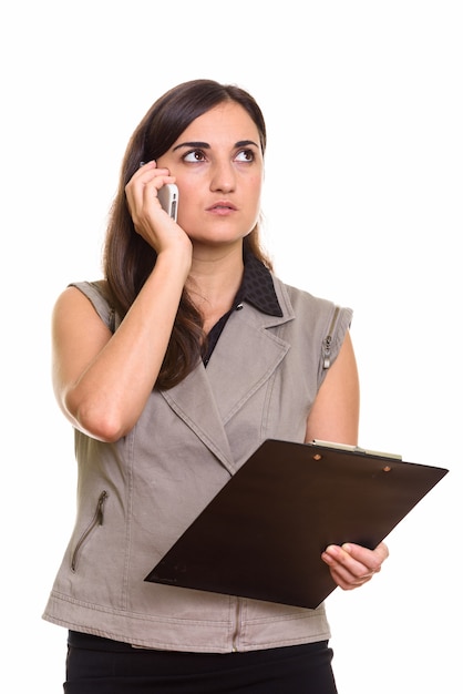 Portrait of young beautiful businesswoman using phone while holding clipboard