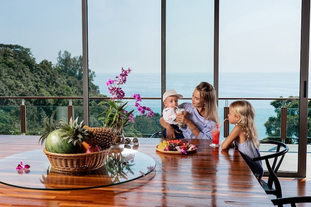 Ritratto di giovane bella madre di famiglia caucasica e i suoi due simpatici bambini seduti al tavolo della cucina a casa e fare colazione insieme vacanze estive