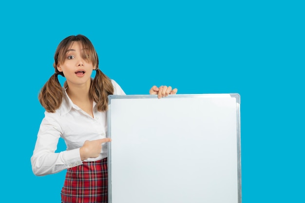 Portrait of young beautiful college girl holding white idea board and point finger on it. High quality photo