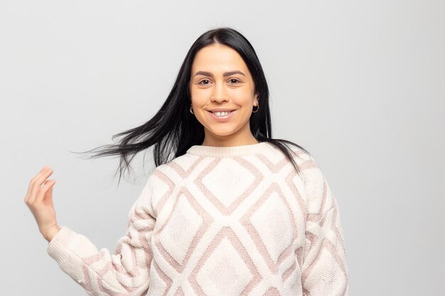 Portrait of a young beautiful cute brunette girl in a warm winter sweater on light gray background