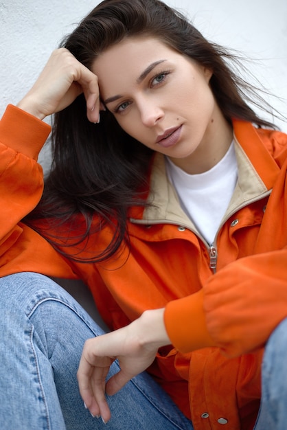 Portrait of young beautiful fashionable female hipster in red summer jacket near white wall