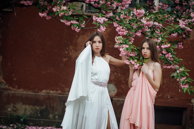 Portrait of young beautiful fashionable girl posing near blooming tree with pink flowers.