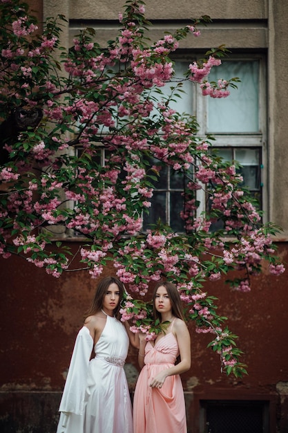 Portrait of young beautiful fashionable girl posing near blooming tree with pink flowers.