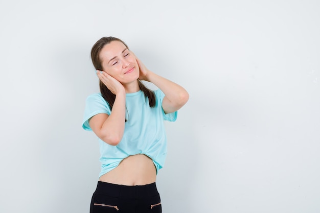 Portrait of young beautiful female covering ears with hands in t-shirt and looking merry front view