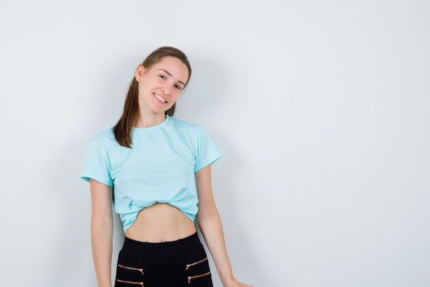 Portrait of young beautiful female looking at camera in t-shirt, pants and looking blissful front view