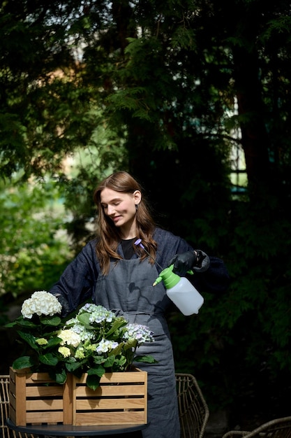 Portrait of a young beautiful florist in an apron watering plants in a pot in the garden