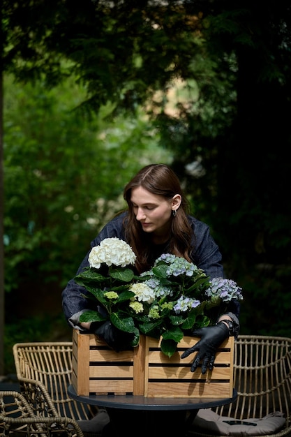 Portrait of a young beautiful florist hugging a bouquet of beautiful flowers in a wooden pot on the table in the garden