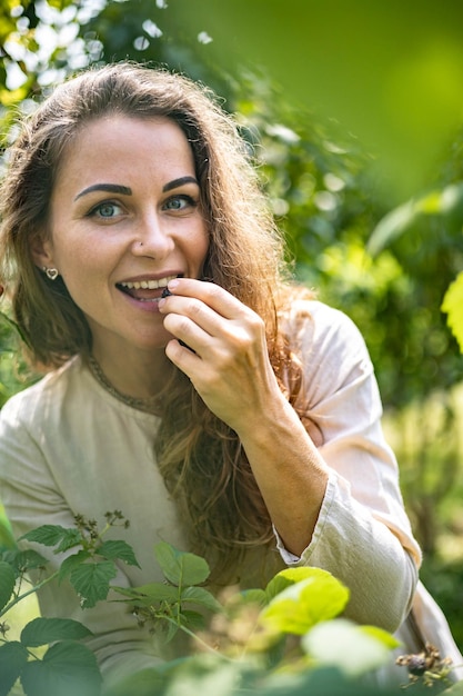 Portrait of young beautiful girl picks blackberries and raspberries in the garden