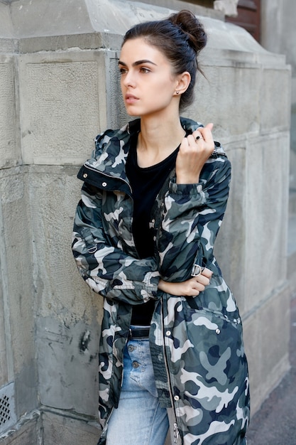 Portrait of young beautiful girl posing on street with camo coat