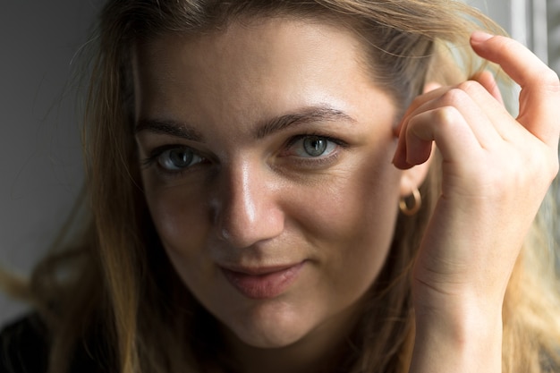 Portrait of a young beautiful girl in a room on a background of a gray wall with shadows, natural light from the window.