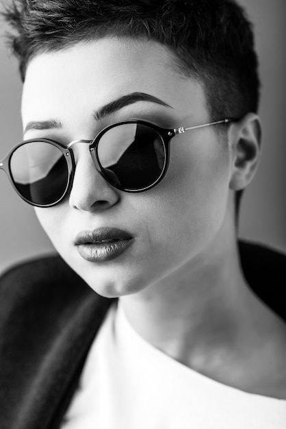 Portrait of a young beautiful girl in sunglasses against a dark background. Black and white