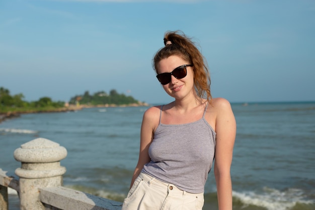 Portrait young beautiful girl in sunglasses on background embankment with sea ocean and island view