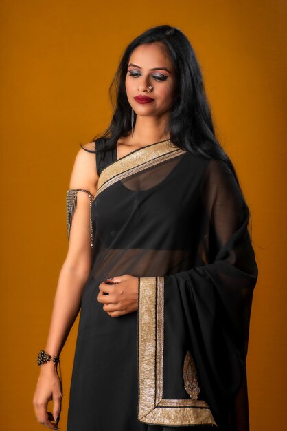 Portrait of a young beautiful girl wearing traditional black saree posing on a brown background