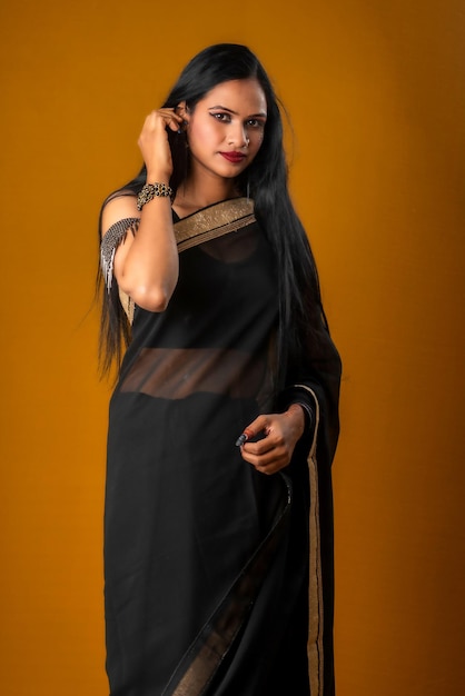 Portrait of a young beautiful girl wearing traditional black saree posing on a brown background