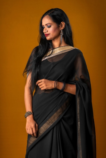 Portrait of a young beautiful girl wearing traditional black saree posing on a brown background