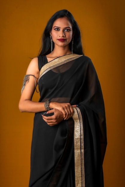 Portrait of a young beautiful girl wearing traditional black saree posing on a brown background