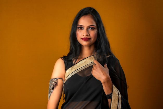 Portrait of a young beautiful girl wearing traditional black saree posing on a brown background