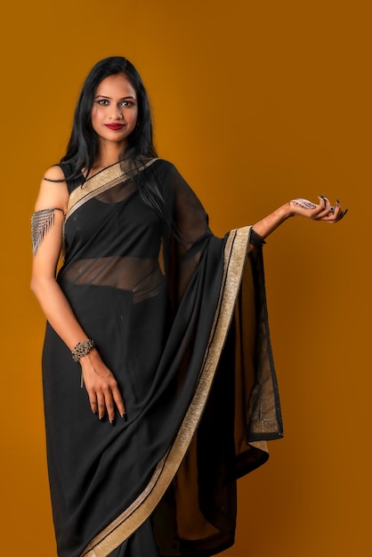 Portrait of a young beautiful girl wearing traditional black saree posing on a brown background