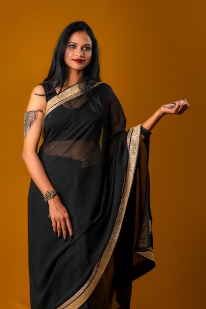 Portrait of a young beautiful girl wearing traditional black saree posing on a brown background