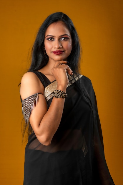 Portrait of a young beautiful girl wearing traditional black saree posing on a brown background