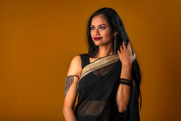 Portrait of a young beautiful girl wearing traditional black saree posing on a brown background