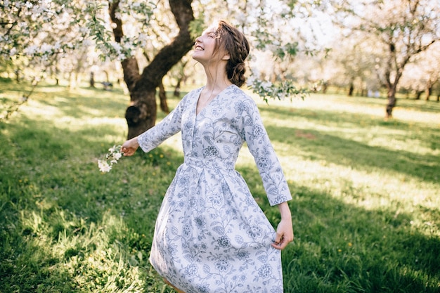 Portrait of young beautiful girl in white lace dress in apple garden, in the tree crown, fingers near mouth