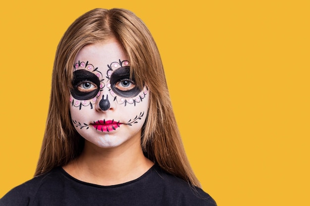 Portrait of young beautiful girl with makeup skeleton on her\
face in yellow studio background