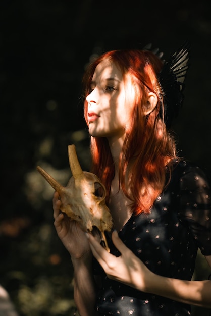 Photo portrait of a young beautiful girl with red hair in nature with bird wings on her head