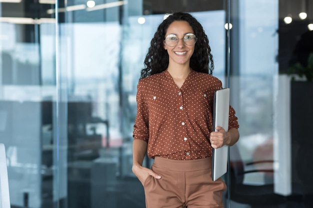 Portrait of young beautiful hispanic female student with laptop woman at work in modern university