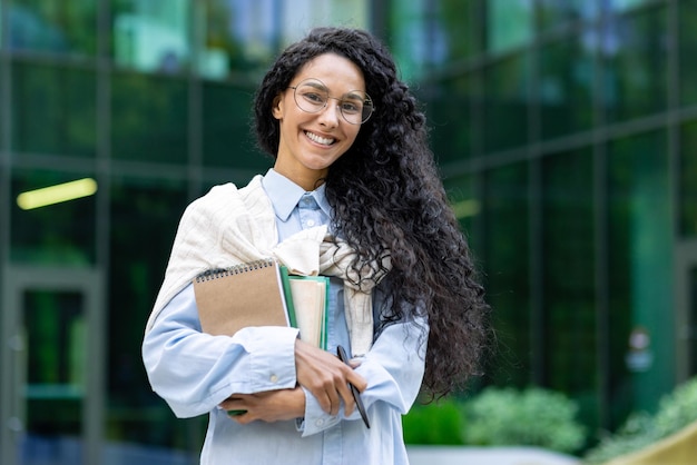 Portrait of a young beautiful hispanic female student woman outside a university campus smiling and