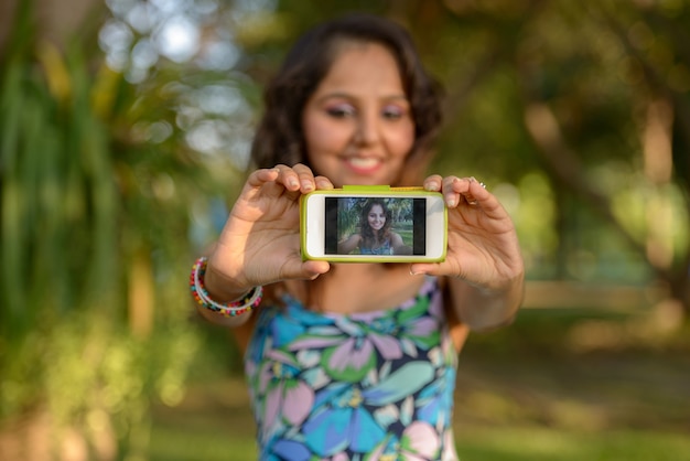 Portrait of young beautiful Indian woman relaxing at the park outdoors