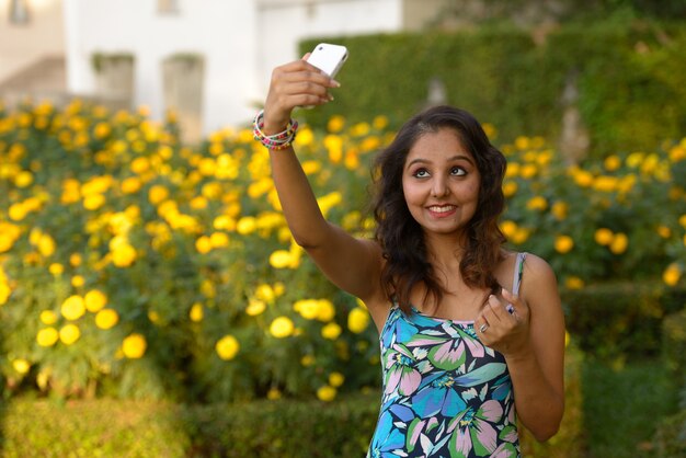 Portrait of young beautiful Indian woman relaxing at the park outdoors