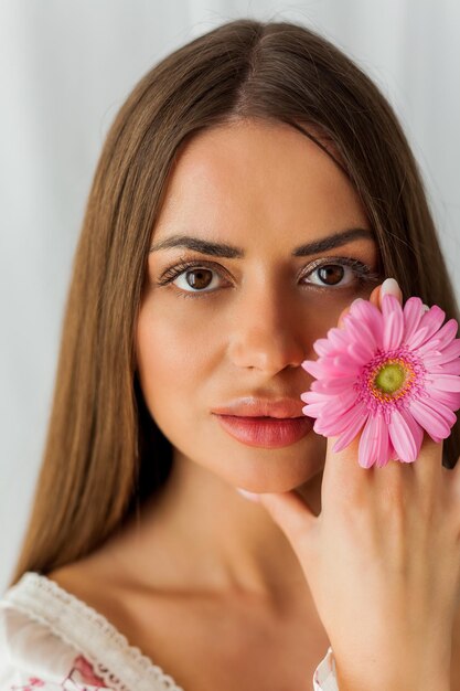 Portrait of young beautiful longhaired browneyed woman with pink gerbera on white background Spring Holidays Mothers Day