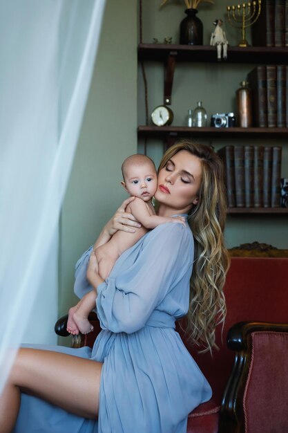 Portrait of young beautiful mother wearing luxury grey dress holding her baby on hands