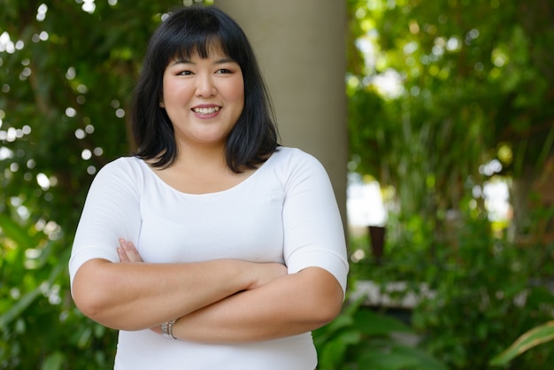 Portrait of young beautiful overweight Asian woman at the park outdoors