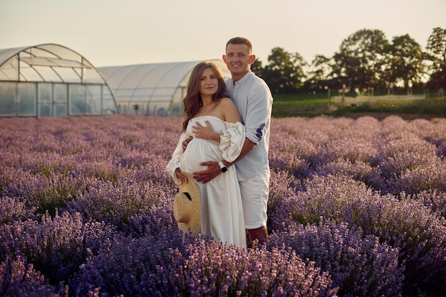 Portrait of a young beautiful pregnant couple on a lavender field at sunset Happy family concept