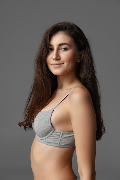 Portrait of young beautiful pregnant woman in lingerie posing isolated over gray studio background.