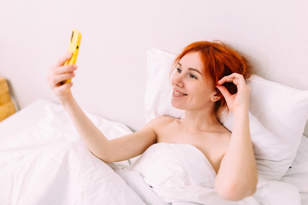 Portrait of a young beautiful redhead woman talking on the phone in bed